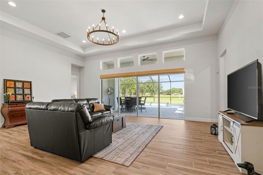 A living room features a black leather sofa, wood-look tile floors, and sliding glass doors — 34653 HEAVENLY LANE, DADE CITY, FL