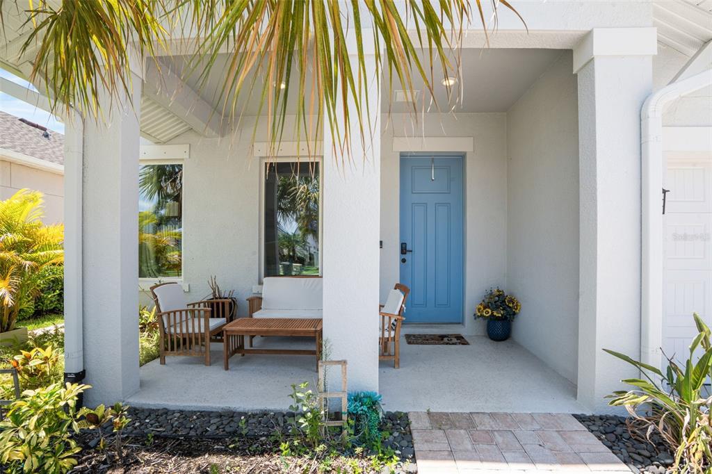 A covered front porch features a blue door, patio furniture, and a stone walkway — 5285 TWINFLOWER LANE, SARASOTA, FL