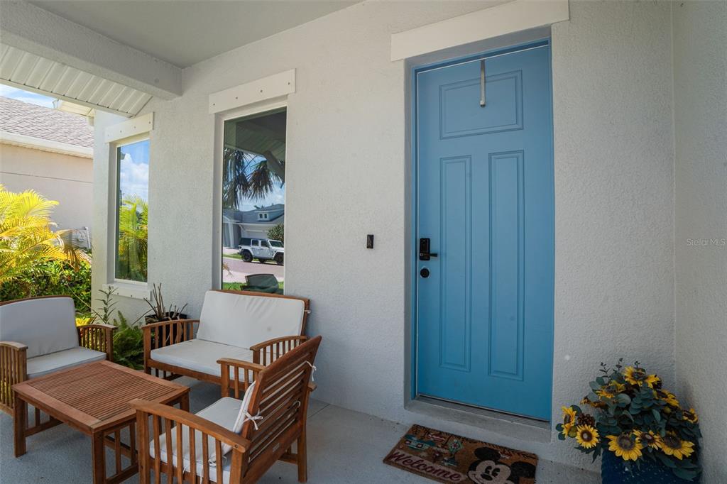 A covered front porch features a blue door, patio furniture, and a Mickey Mouse doormat — 5285 TWINFLOWER LANE, SARASOTA, FL