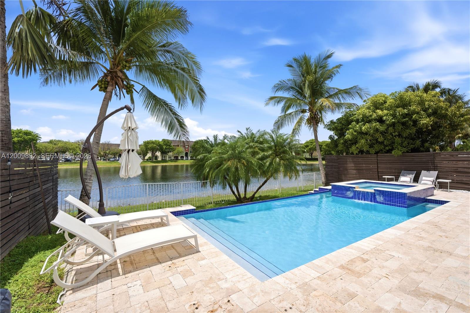 A swimming pool and hot tub sit on a stone patio overlooking a lake — 11090 NW 84th St, Doral FL 33178, DORAL, FL