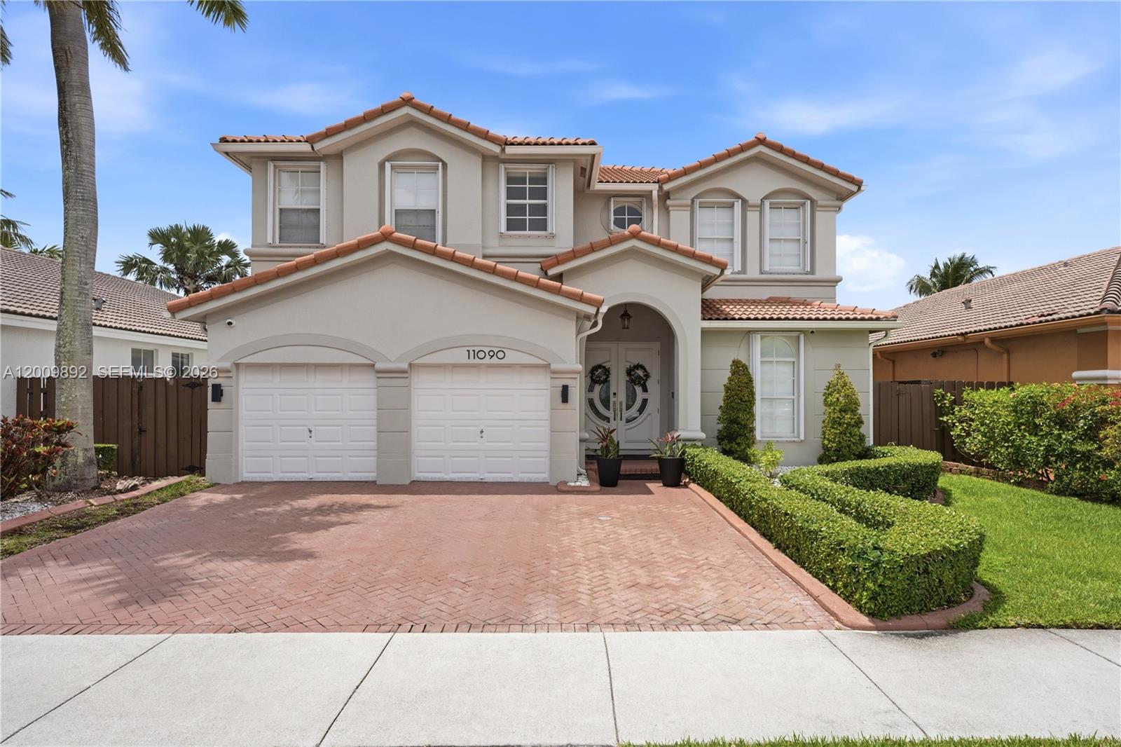 A two-story house features a two-car garage, a tiled roof, and a brick driveway — 11090 NW 84th St, Doral FL 33178, DORAL, FL