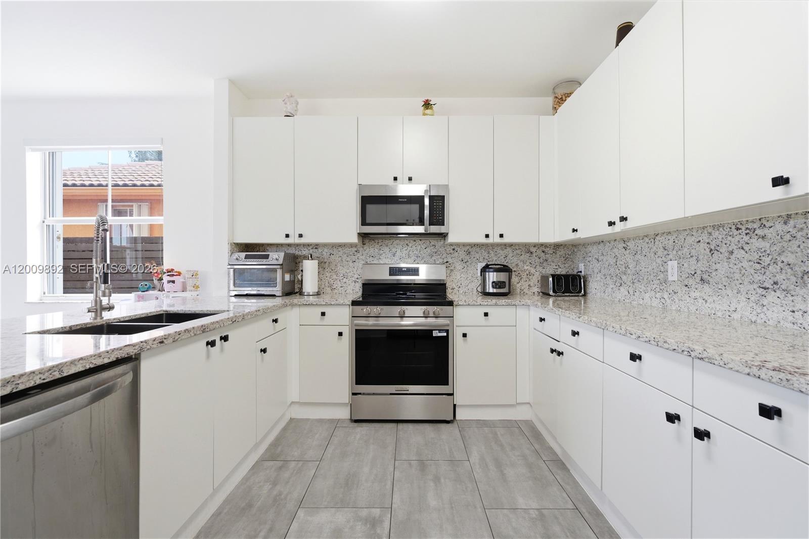 A modern kitchen features white cabinets, granite countertops, stainless steel appliances, and gray tile flooring — 11090 NW 84th St, Doral FL 33178, DORAL, FL
