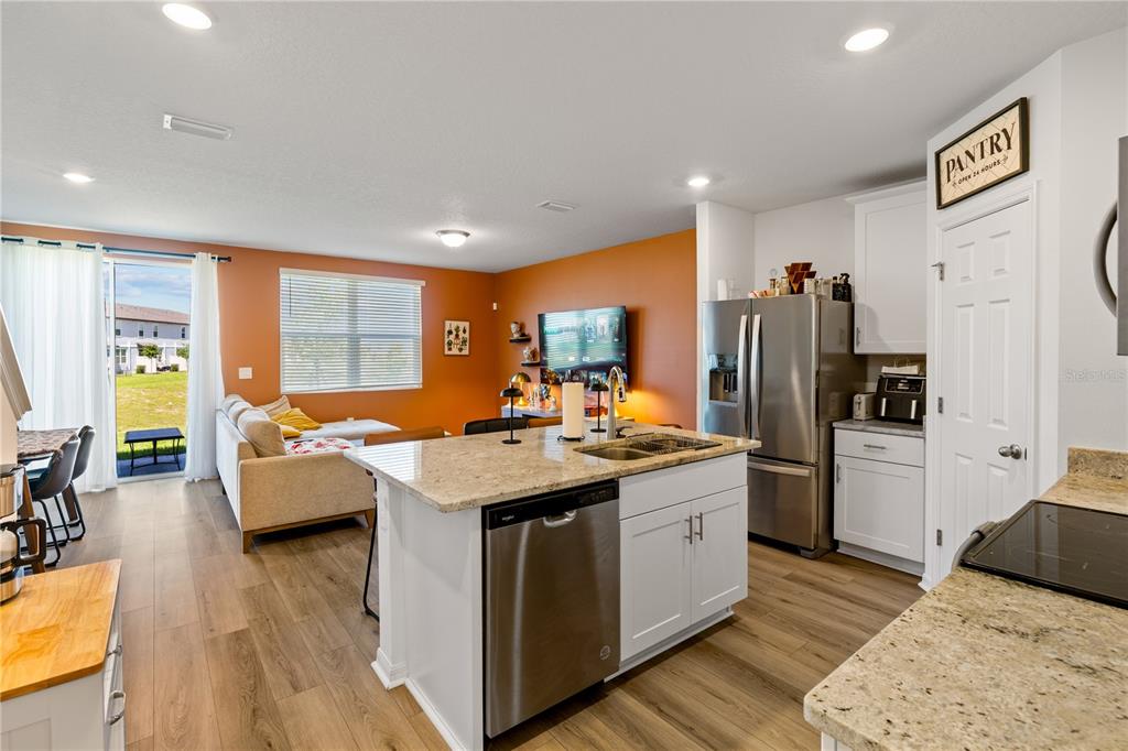 An open-concept kitchen with a granite island overlooks a living area with orange walls — 16320 HAPPY EAGLE DRIVE, CLERMONT, FL