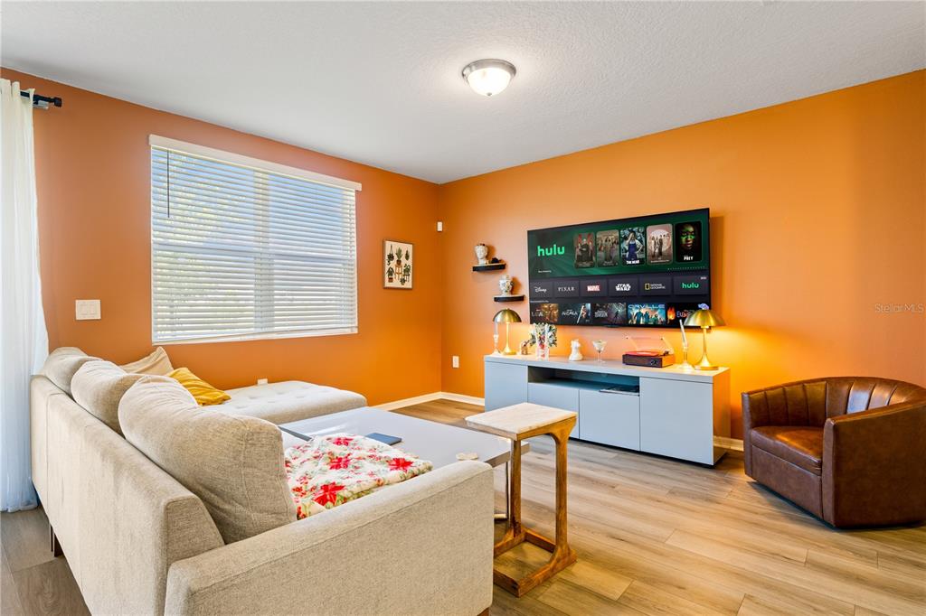 A living room features orange walls, a grey sectional sofa, a television, and wood flooring — 16320 HAPPY EAGLE DRIVE, CLERMONT, FL