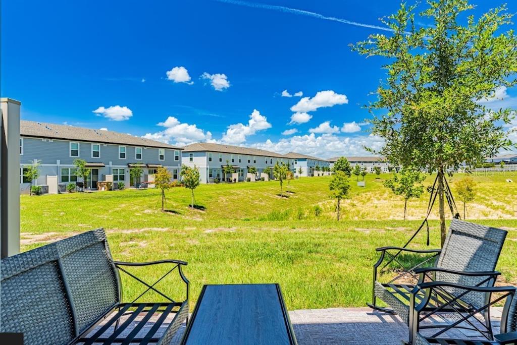 A patio with outdoor furniture overlooks a grassy lawn and neighboring townhomes under a blue sky — 16320 HAPPY EAGLE DRIVE, CLERMONT, FL