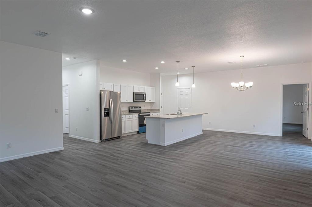 An open-concept kitchen and living area featuring white cabinets, stainless steel appliances, and gray flooring — 561 WILDMER ROAD SW, PALM BAY, FL