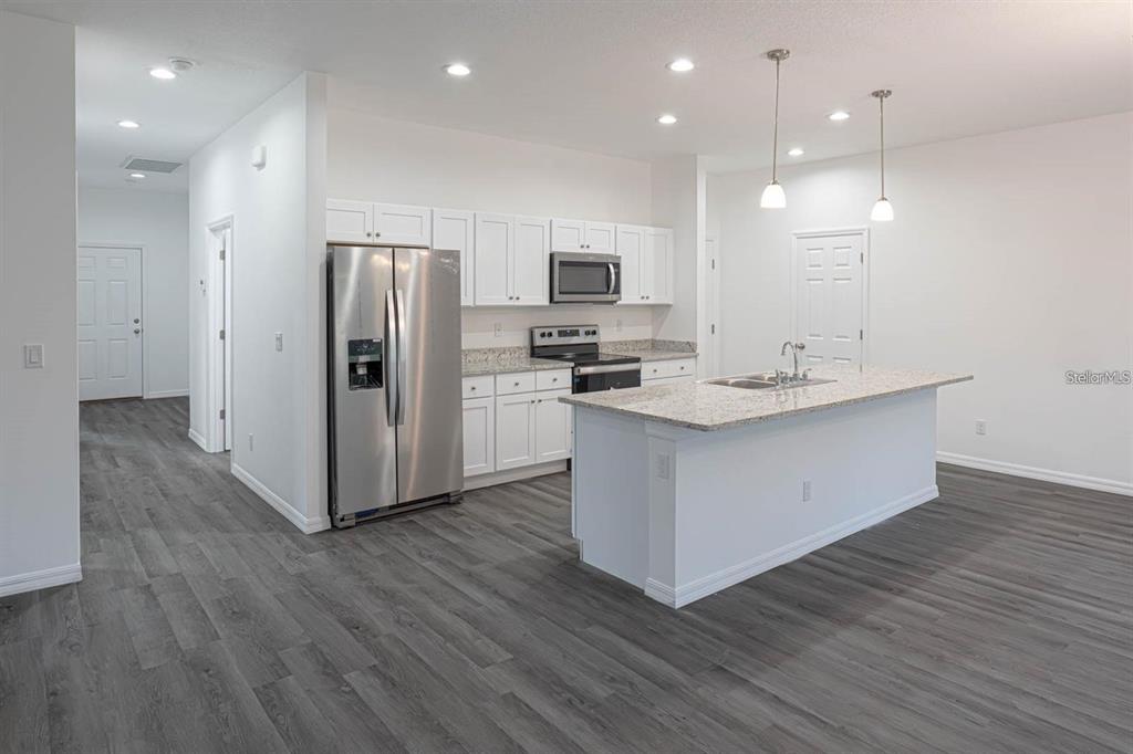 A kitchen features white cabinets, stainless steel appliances, a granite island, and gray wood-look flooring — 561 WILDMER ROAD SW, PALM BAY, FL