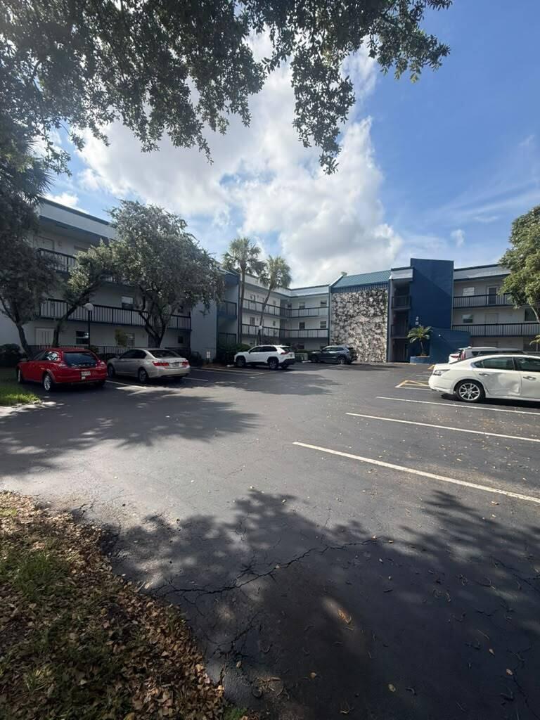 An exterior view of a multi-story apartment complex with a parking lot in front — 3210 Holiday Springs Boulevard # 103, Margate FL 33063, MARGATE, FL