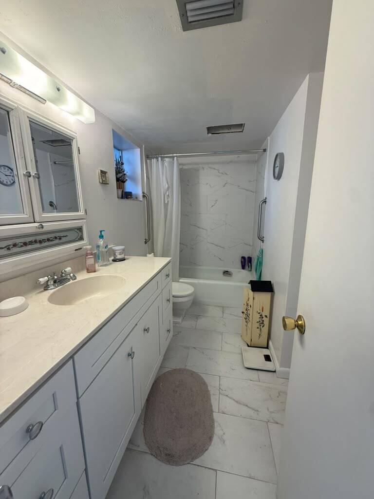 A bathroom features a white vanity, a marble-tiled shower-tub combination, and light-colored floor tiles — 3210 Holiday Springs Boulevard # 103, Margate FL 33063, MARGATE, FL