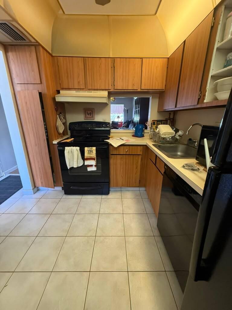 A kitchen with wood-tone cabinets, black appliances, white tile flooring, and a pass-through window — 3210 Holiday Springs Boulevard # 103, Margate FL 33063, MARGATE, FL