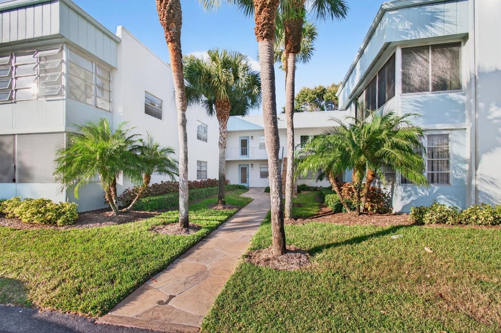 A paved walkway leads between two white apartment buildings surrounded by palm trees and grass — 449 Normandy J, Delray Beach FL 33484, DELRAY BEACH, FL