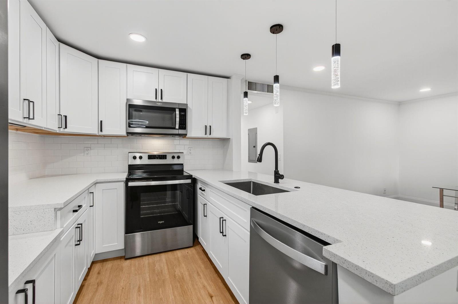 A modern kitchen features white cabinets, stainless steel appliances, quartz countertops, and a breakfast bar — 449 Normandy J, Delray Beach FL 33484, DELRAY BEACH, FL