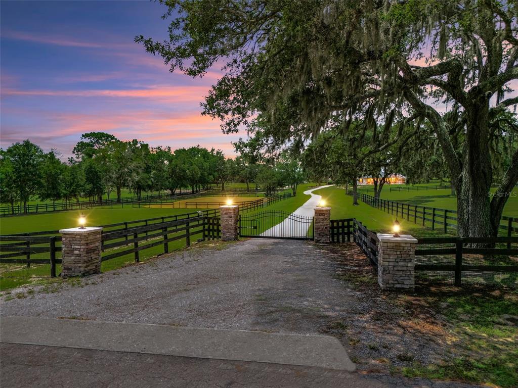 A gravel driveway leads through a gated entrance with stone pillars to a rural property — 14356 SW 101ST LANE, DUNNELLON, FL