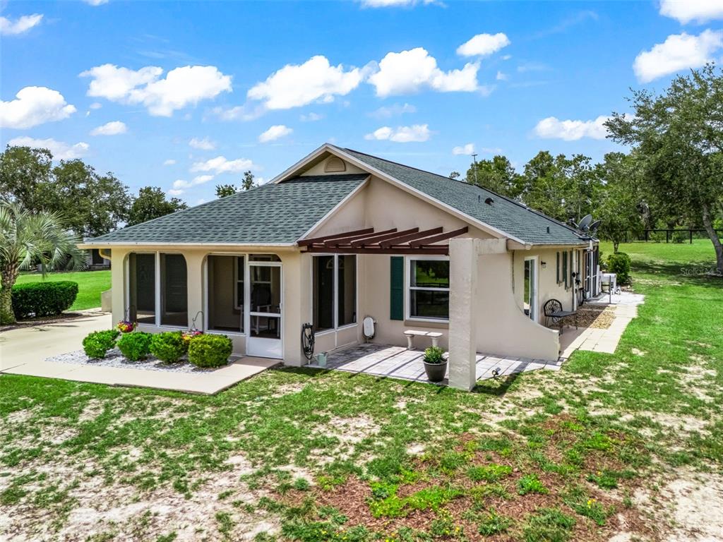 A beige house with a green shingled roof, a screened porch, and a wooden pergola — 14356 SW 101ST LANE, DUNNELLON, FL
