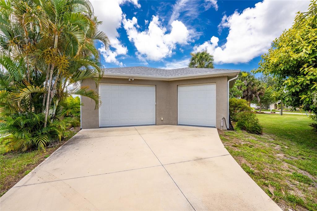 A tan house exterior features two white garage doors and a concrete driveway — 5105 ACKLEY TERRACE, PORT CHARLOTTE, FL