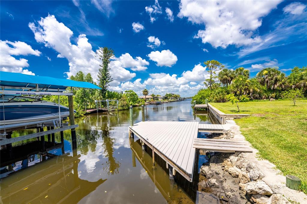 A boat lift and a wooden dock sit along a canal with grassy banks — 5105 ACKLEY TERRACE, PORT CHARLOTTE, FL