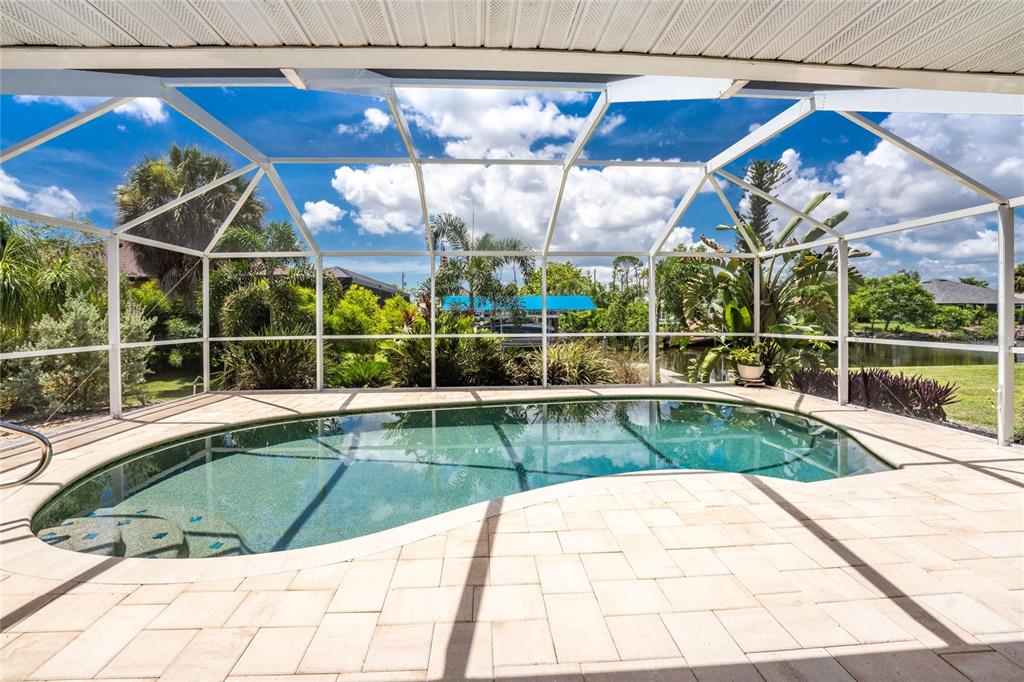 A screened-in swimming pool with a paver deck overlooks a canal and lush tropical landscaping — 5105 ACKLEY TERRACE, PORT CHARLOTTE, FL