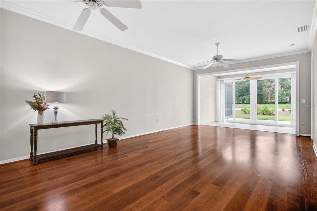 A spacious living room features hardwood floors, a console table, and sliding glass doors to outside — 6948 STONEYWALK COURT, BRADENTON, FL