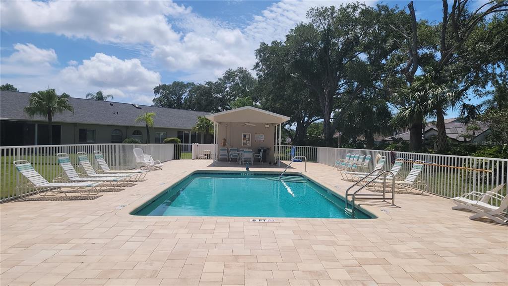 A rectangular swimming pool with a covered patio area and lounge chairs on a paved deck — 6948 STONEYWALK COURT, BRADENTON, FL