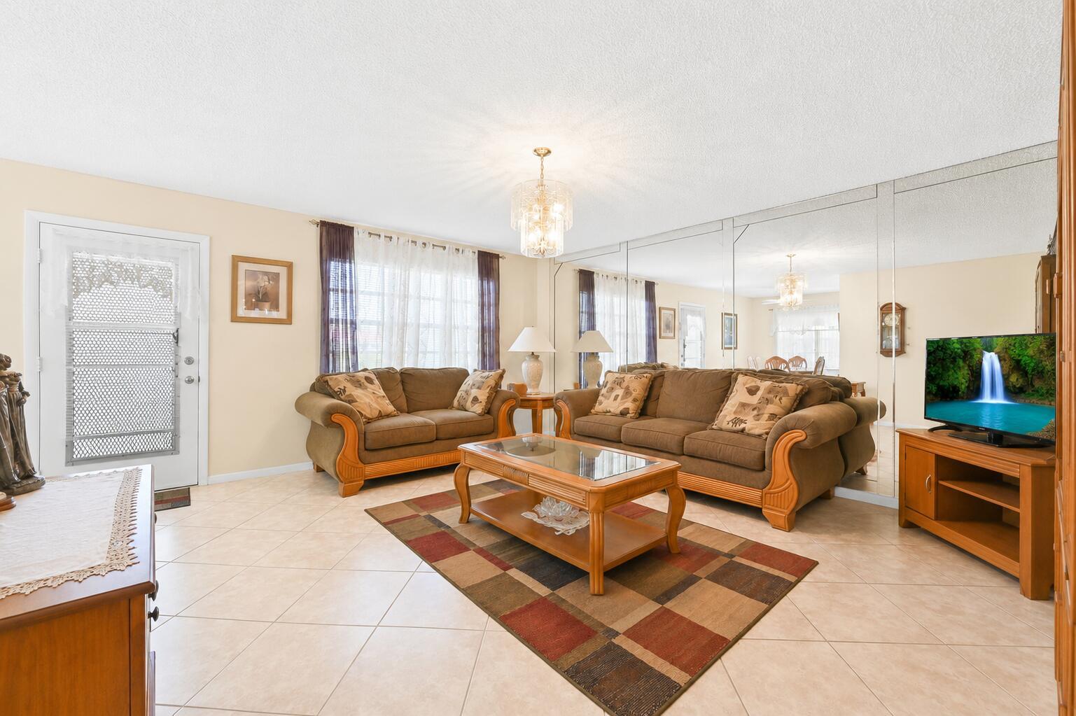 A living room features tile floors, two brown sofas, a coffee table, and mirrored walls — 507 Normandy K, Delray Beach FL 33484, DELRAY BEACH, FL