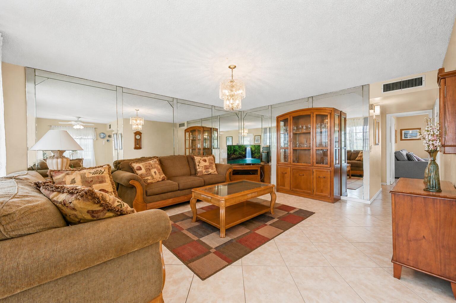 A living room features a mirrored wall, brown sofas, a coffee table, and tile flooring — 507 Normandy K, Delray Beach FL 33484, DELRAY BEACH, FL