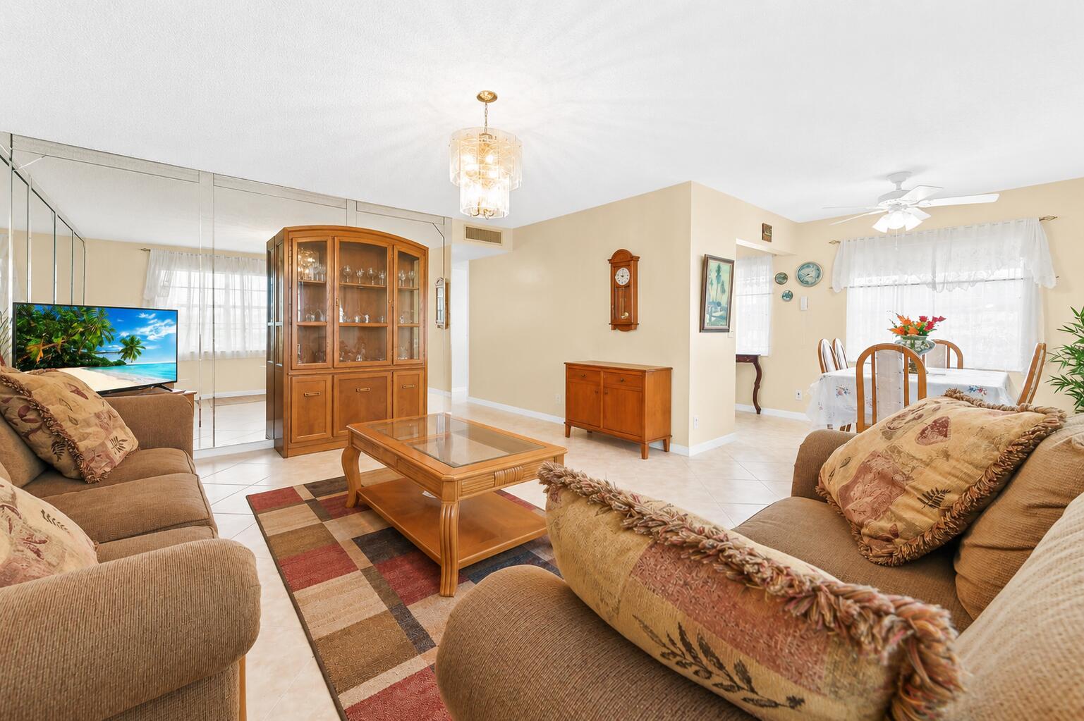 A living room with beige sofas, a glass-top coffee table, and a large mirrored wall — 507 Normandy K, Delray Beach FL 33484, DELRAY BEACH, FL