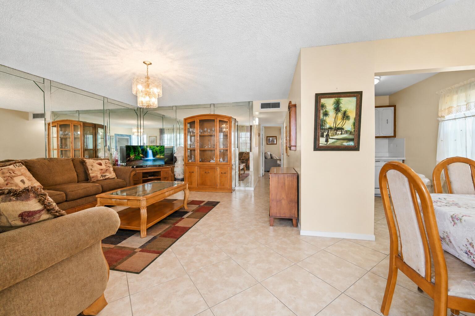 A living room with tiled floors, a mirrored wall, and a dining area nearby — 507 Normandy K, Delray Beach FL 33484, DELRAY BEACH, FL