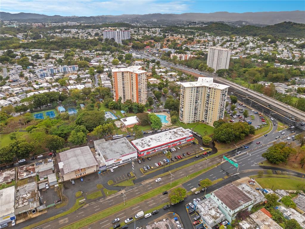 An aerial view shows two high-rise apartment buildings, a commercial strip, and a multi-lane highway — 65 Avenida de Infanteria CONCORDIA GARDENS SHOPPING CENTER ANNEX BULDING AVENUE, SAN JUAN, PR