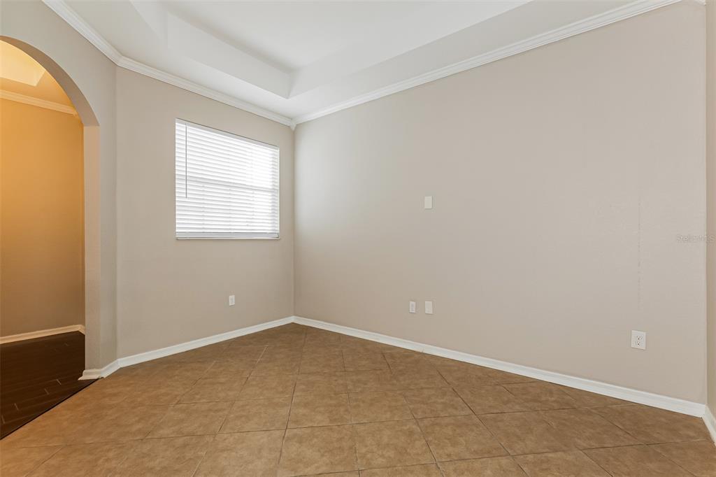 An empty room with beige walls, a tray ceiling, and brown tile flooring — 8130 WOODVINE CIRCLE, LAKELAND, FL