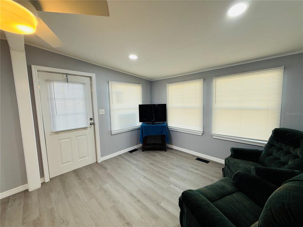 A living room features light gray walls, wood-look flooring, a white door, and a dark recliner — 4851 W GANDY BOULEVARD UNIT B7L27, TAMPA, FL