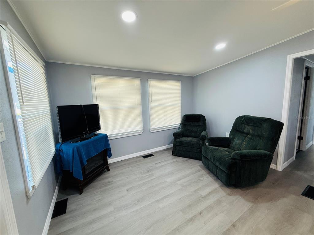 A living room with light gray walls, wood-look flooring, two dark green recliners, and a television — 4851 W GANDY BOULEVARD UNIT B7L27, TAMPA, FL