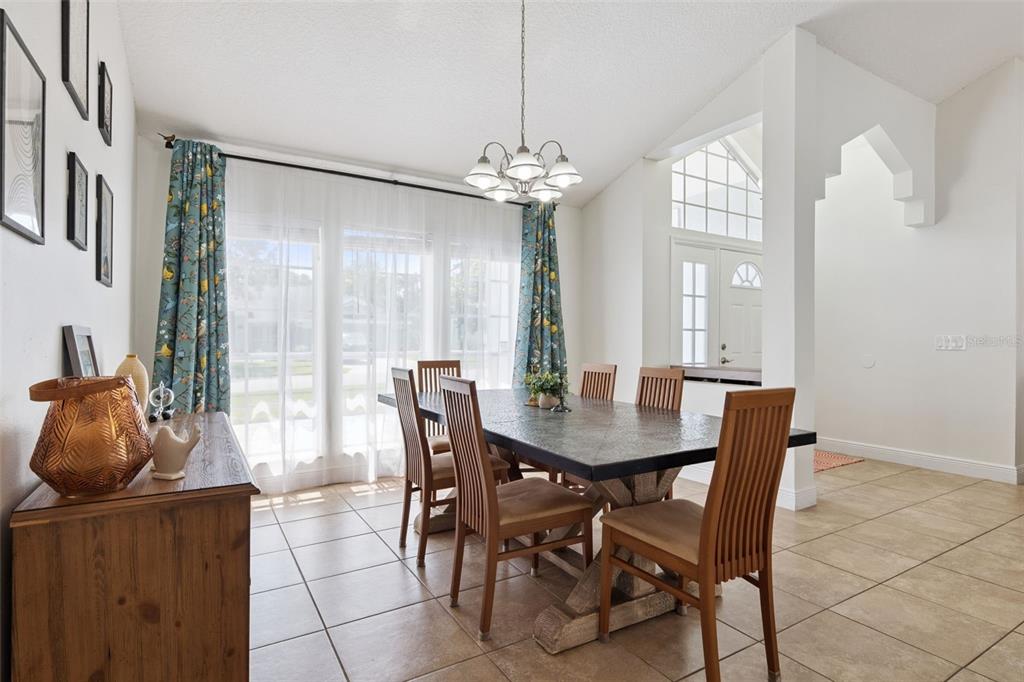 A dining room with a stone-topped table, wooden chairs, tile flooring, and large windows — 1017 TURTLE CREEK DRIVE, OVIEDO, FL