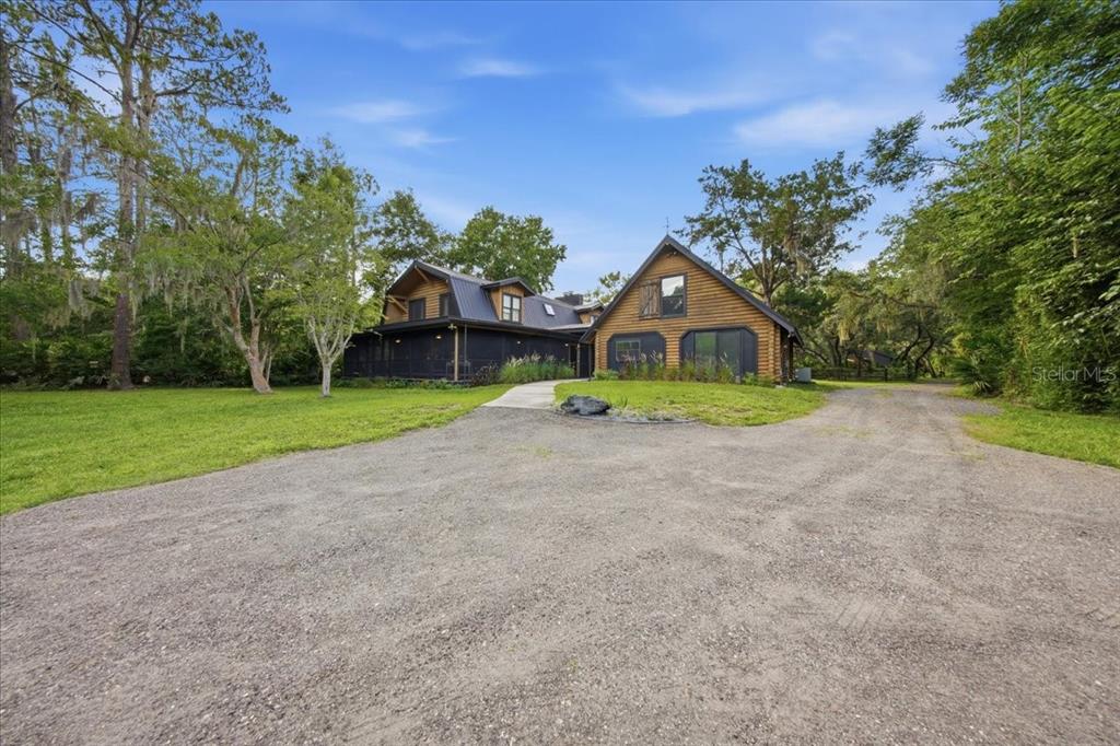 A two-story log cabin sits on a large grassy lot with a gravel driveway — 1630 STILLMEADOW ROAD, DELTONA, FL