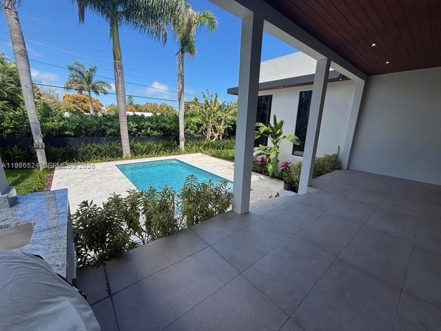 A covered patio overlooks a swimming pool surrounded by palm trees and landscaping — 2161 NE 124th St, North Miami FL 33181, NORTH MIAMI, FL
