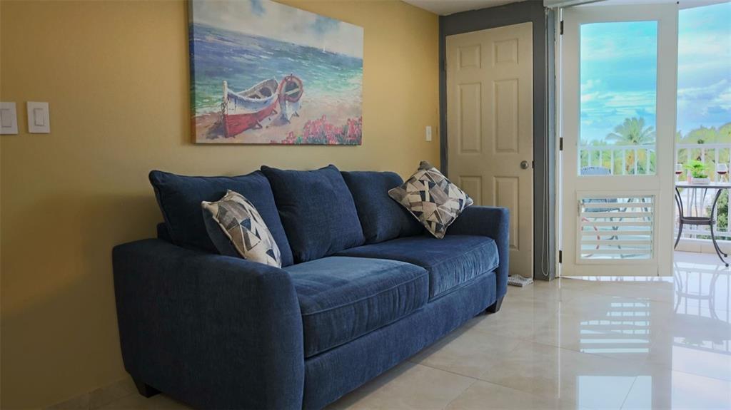 A blue sofa sits in a living room with yellow walls and a balcony view — MARBELLA DEL CARIBE ESTE UNIT 508, CAROLINA, PR