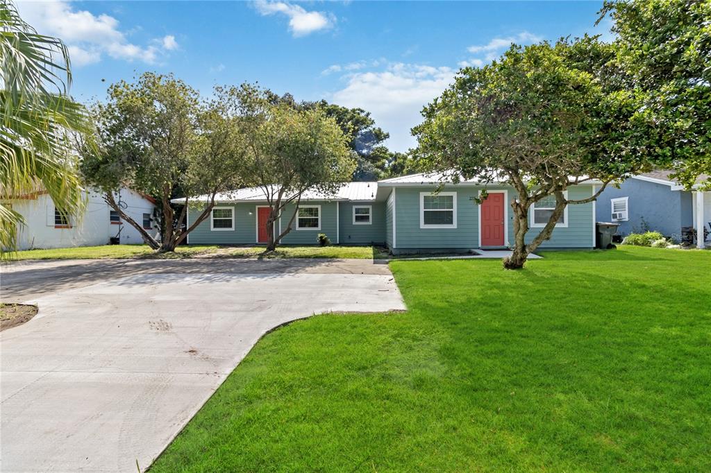 A single-story house with light green siding, two red doors, and a large concrete driveway — 225 MONTANA AVENUE, ST CLOUD, FL