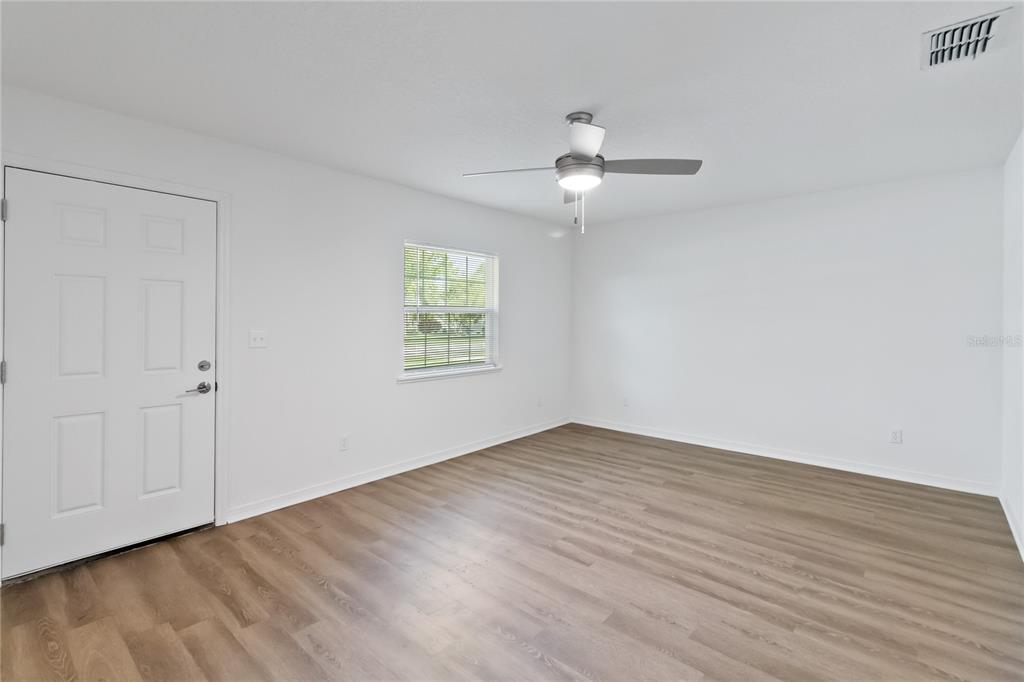 An empty room with white walls, wood-look flooring, a ceiling fan, and a white door — 225 MONTANA AVENUE, ST CLOUD, FL