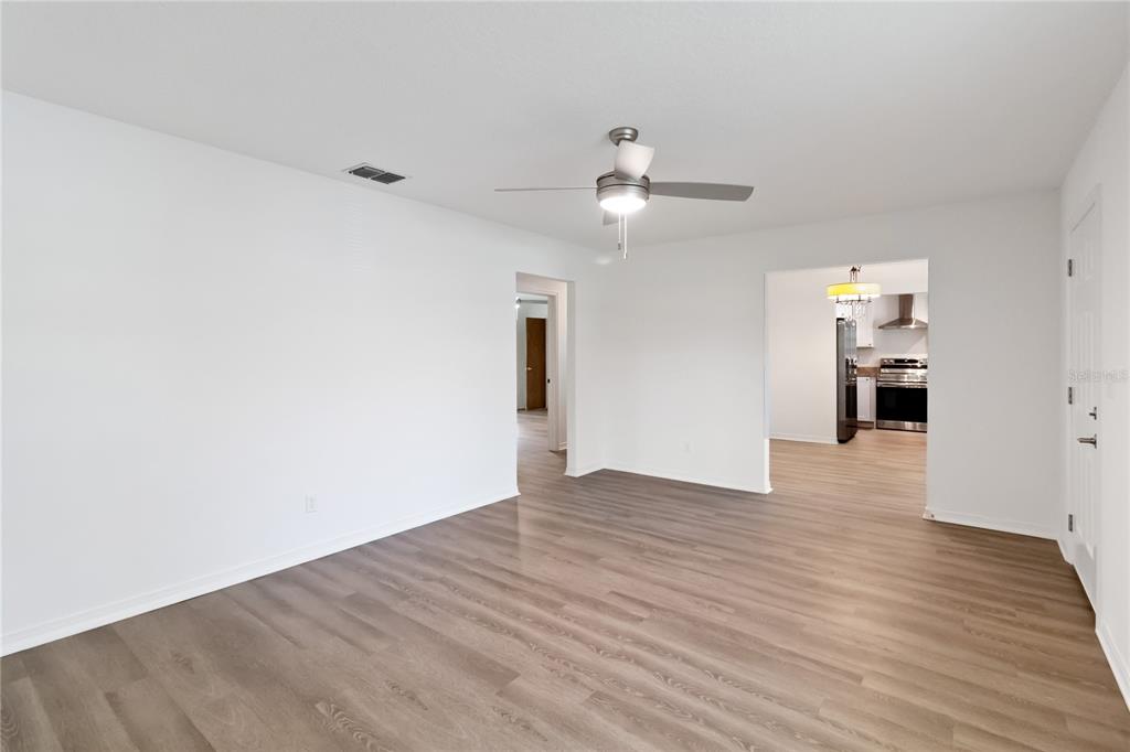 A living room with light wood-look flooring, a ceiling fan, and an adjacent kitchen — 225 MONTANA AVENUE, ST CLOUD, FL