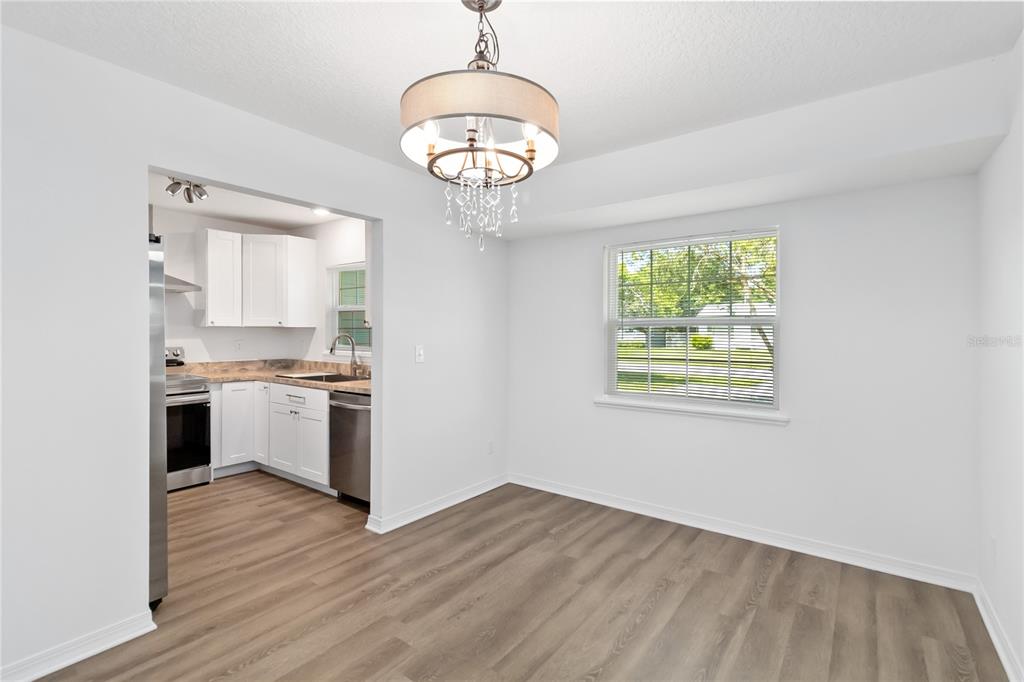 A dining area with wood-look flooring and a chandelier opens into a white kitchen — 225 MONTANA AVENUE, ST CLOUD, FL