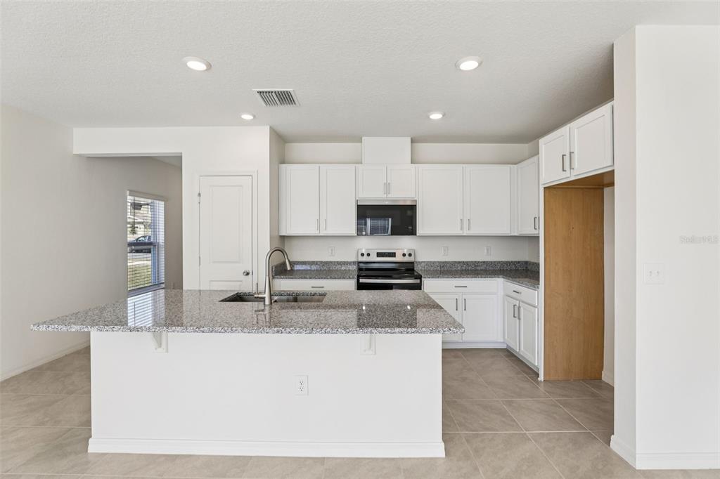 A kitchen features white cabinets, granite countertops, a center island, and stainless steel appliances — 379 SEQUOIA DRIVE, LAKE WALES, FL