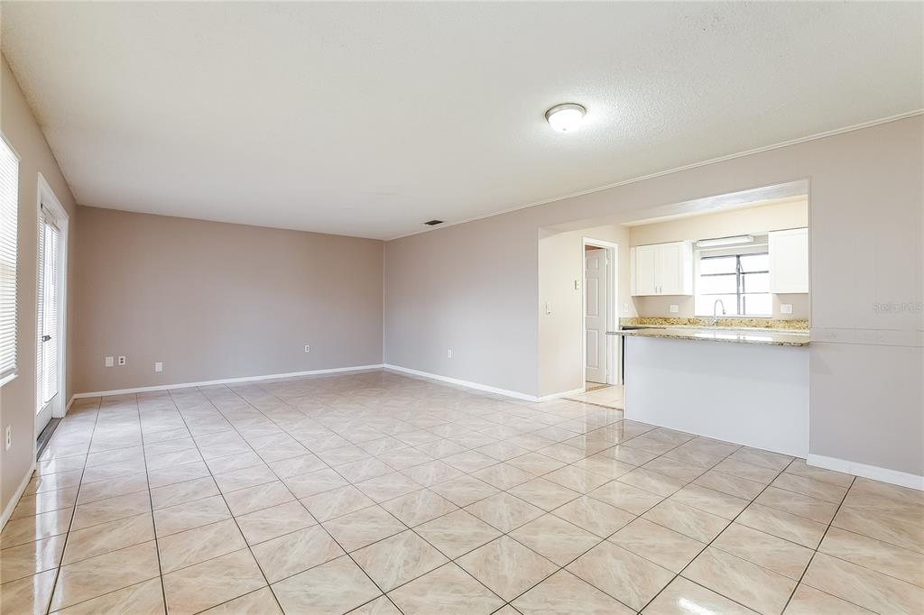 An open-concept living area features light-colored tile flooring, beige walls, and a kitchen pass-through window — 6529 PRECOURT DRIVE, ORLANDO, FL