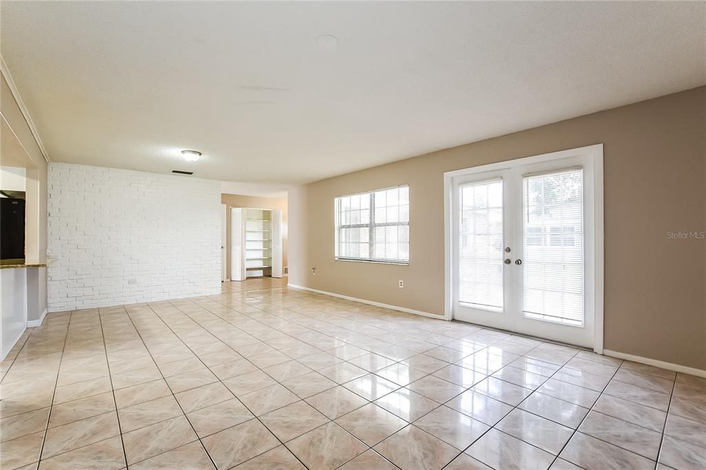 An empty room with beige tile flooring, a white brick accent wall, and glass doors — 6529 PRECOURT DRIVE, ORLANDO, FL