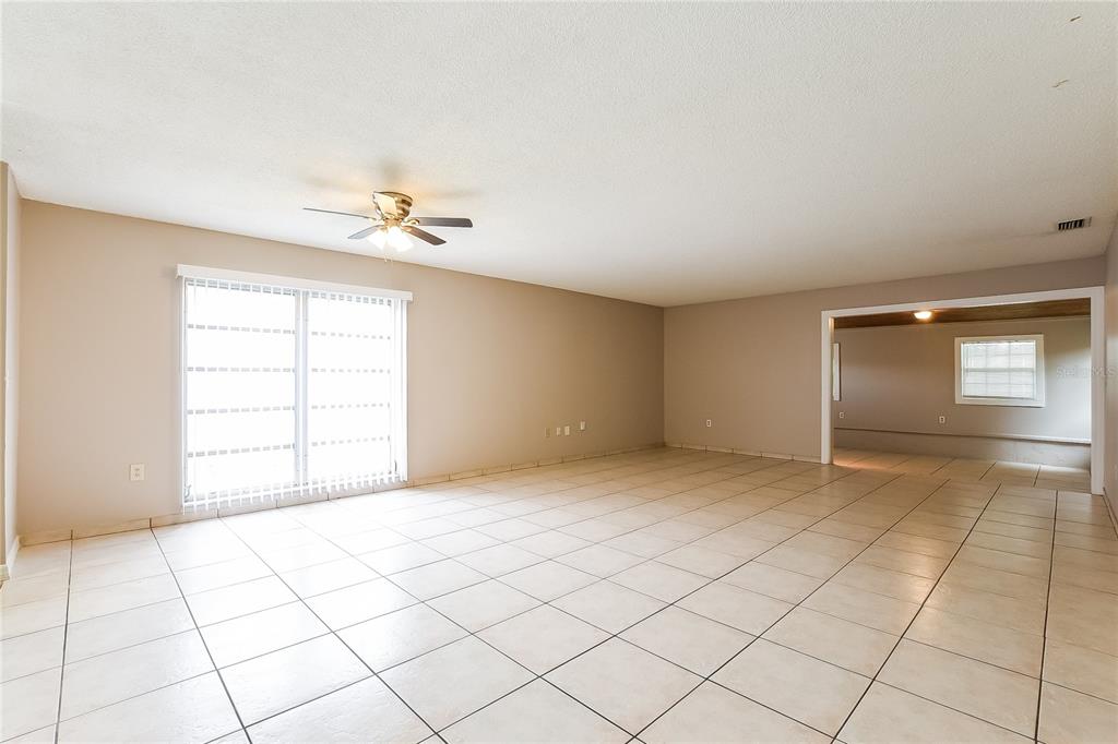 An empty room with beige walls, light-colored tile flooring, a ceiling fan, and sliding doors — 6529 PRECOURT DRIVE, ORLANDO, FL