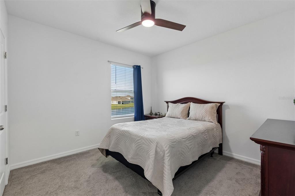 A bedroom features a bed, a ceiling fan, a window with blue curtains, and carpet — 3406 GRASSY KNOLL COURT, PLANT CITY, FL