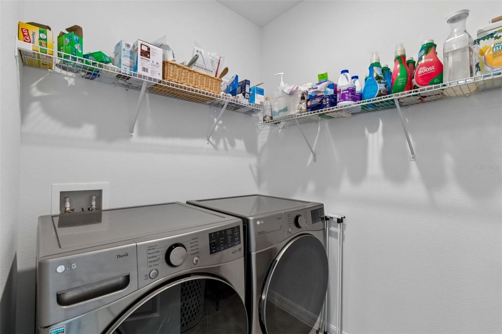 A laundry room features a silver washer and dryer beneath a wire storage shelf — 3406 GRASSY KNOLL COURT, PLANT CITY, FL