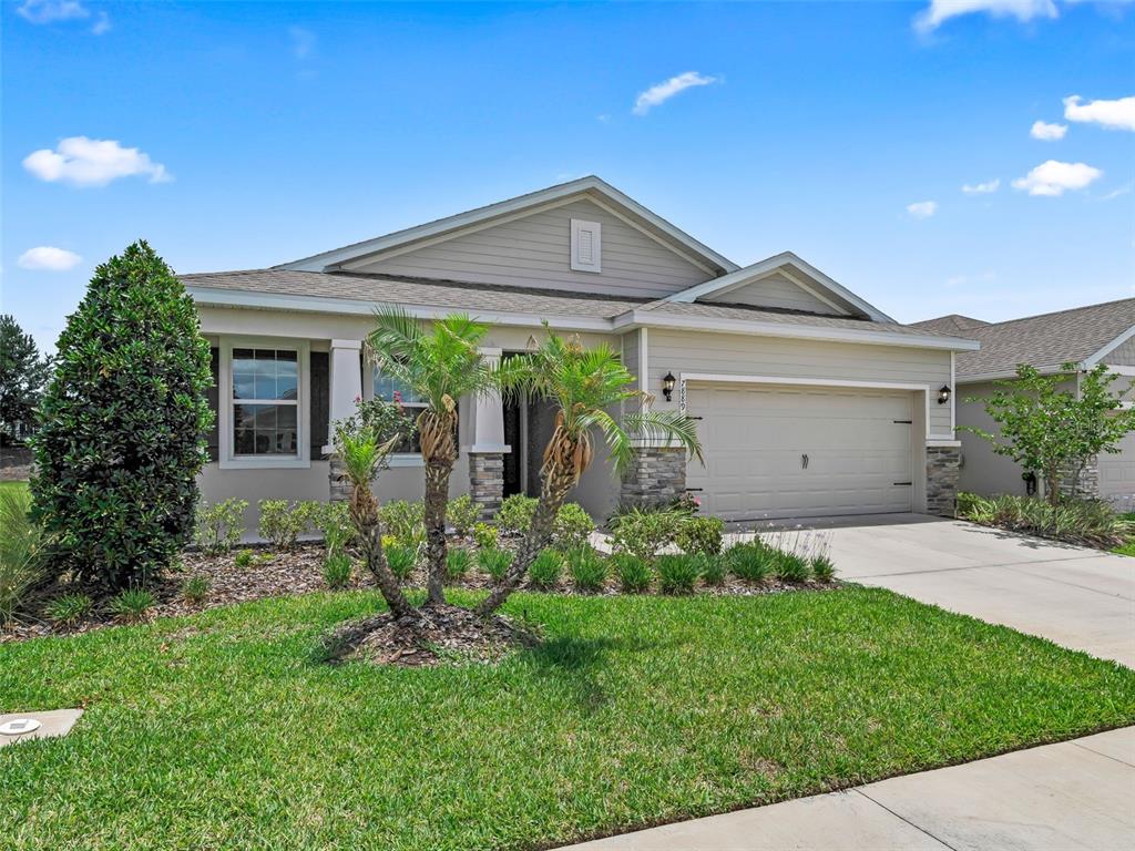 A single-story house with beige siding, a stone-accented entryway, and a two-car garage — 7889 PENROSE PLACE, WILDWOOD, FL