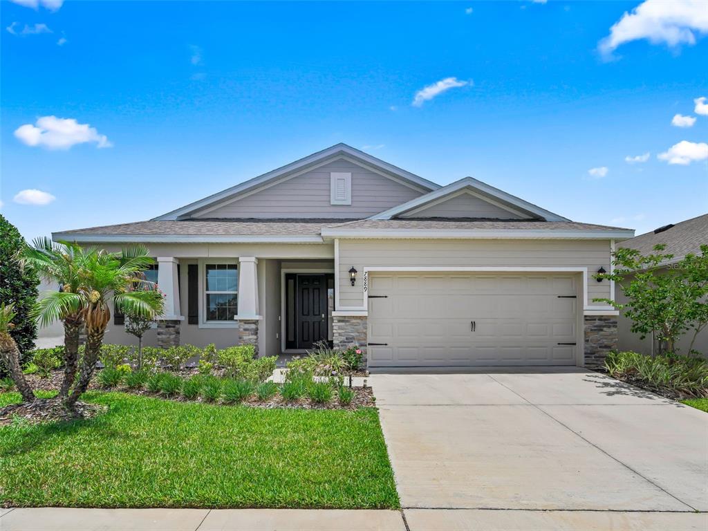 A single-story suburban house features a two-car garage, stone accents, and a landscaped front yard — 7889 PENROSE PLACE, WILDWOOD, FL