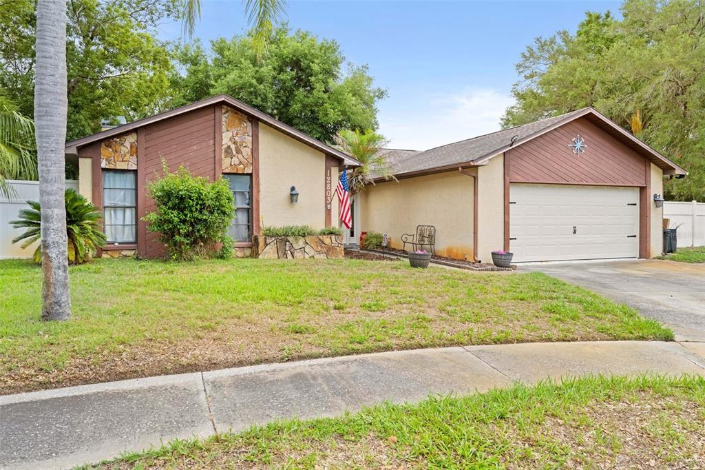 A single-story house with a tan stucco exterior, stone accents, and an attached two-car garage — 12803 RED MAPLE COURT, HUDSON, FL