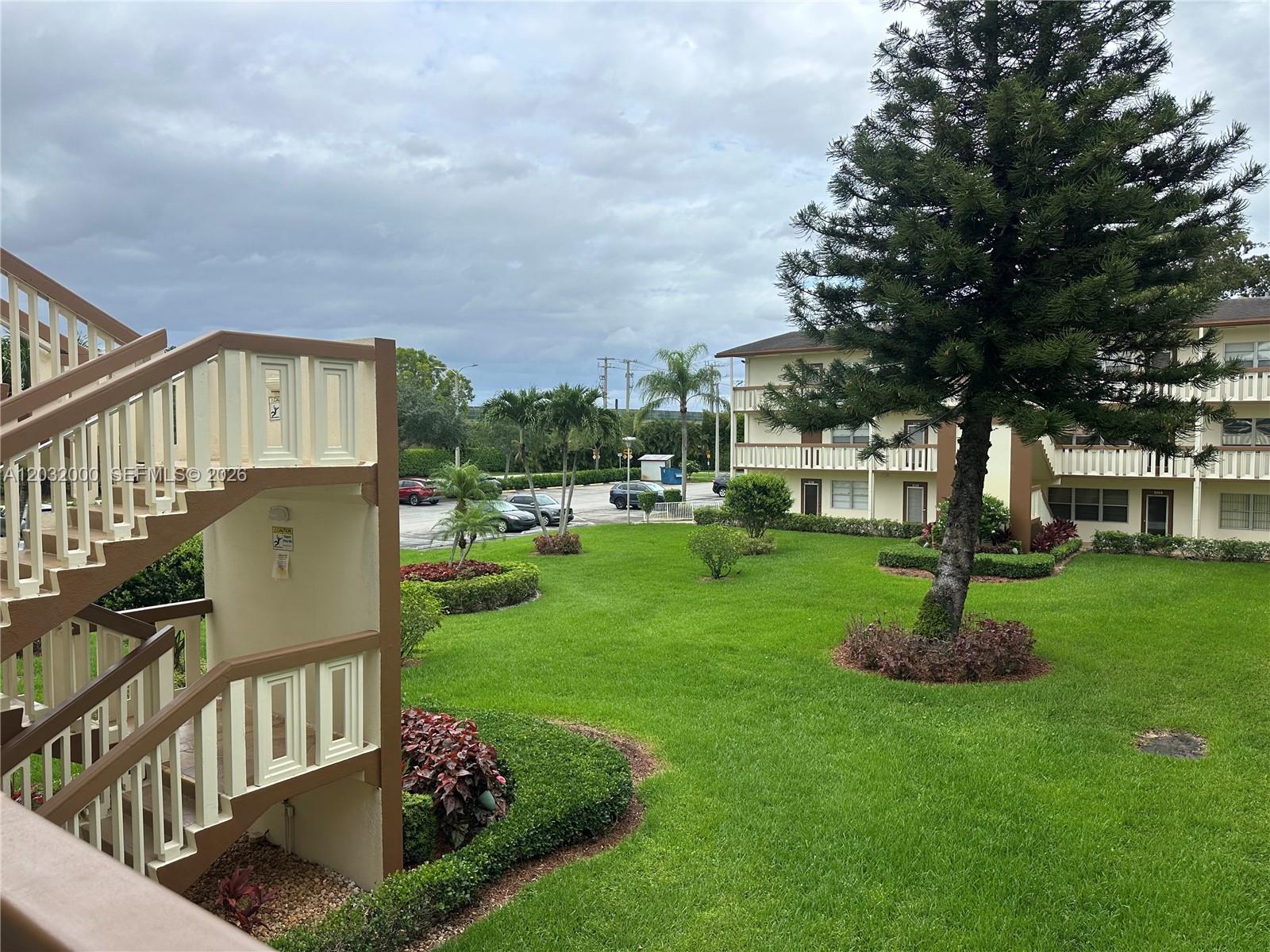 An outdoor view of a grassy courtyard between two apartment buildings with exterior staircases — 445 Mansfield K # 445, Boca Raton FL 33434, BOCA RATON, FL