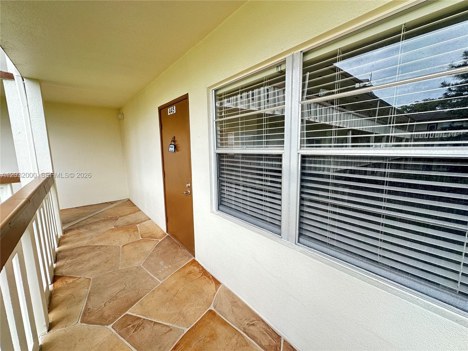 A brown door with a lockbox and a large window face a stone-tiled walkway — 445 Mansfield K # 445, Boca Raton FL 33434, BOCA RATON, FL